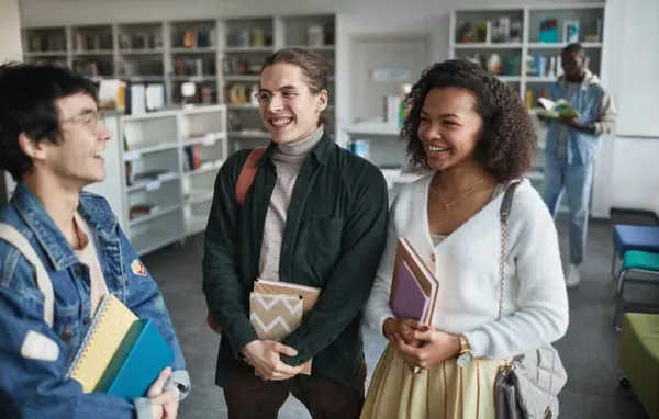 Group of diverse students laughing and holding books in a library environment.