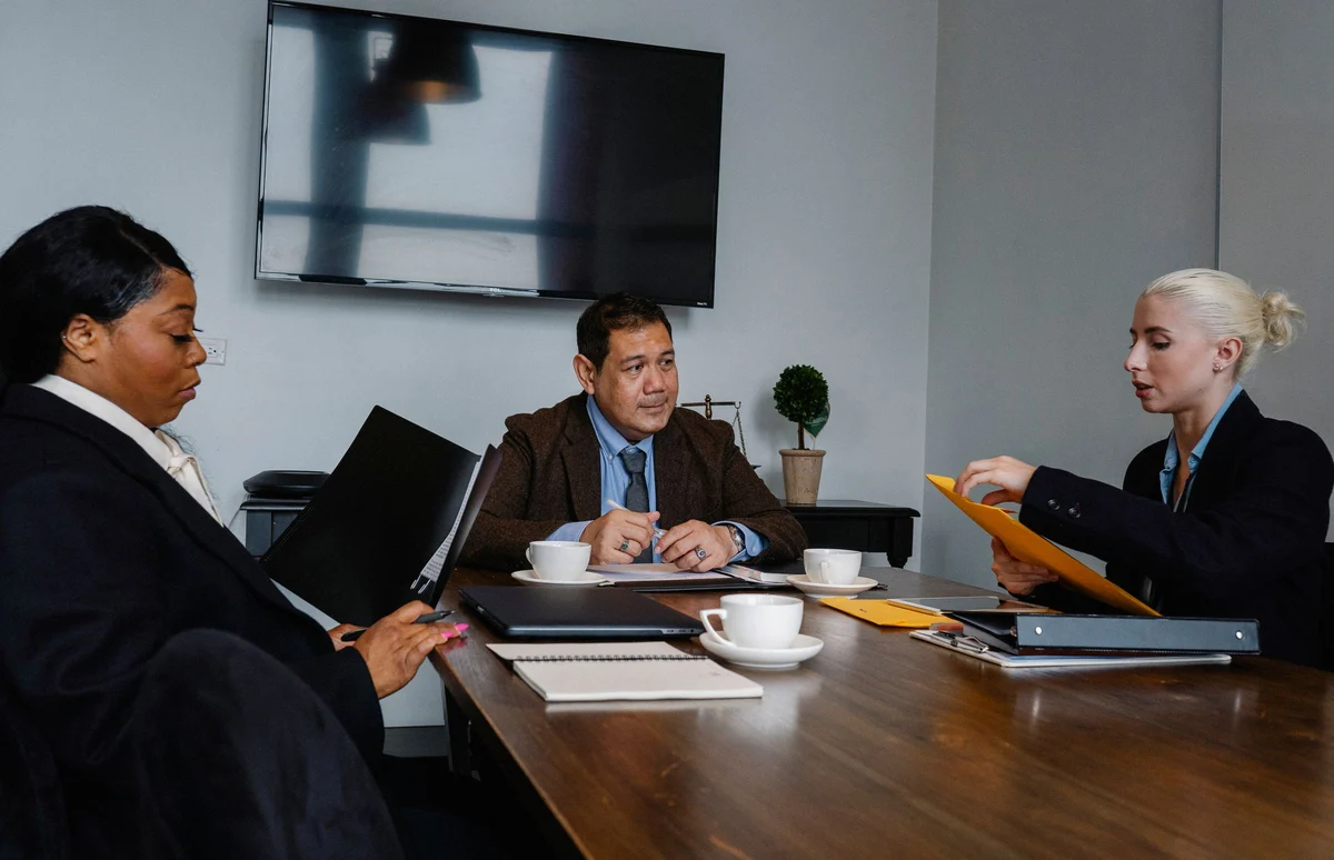 Group of multiethnic coworkers in formal wear sitting at table with documents and discussing strategy of project