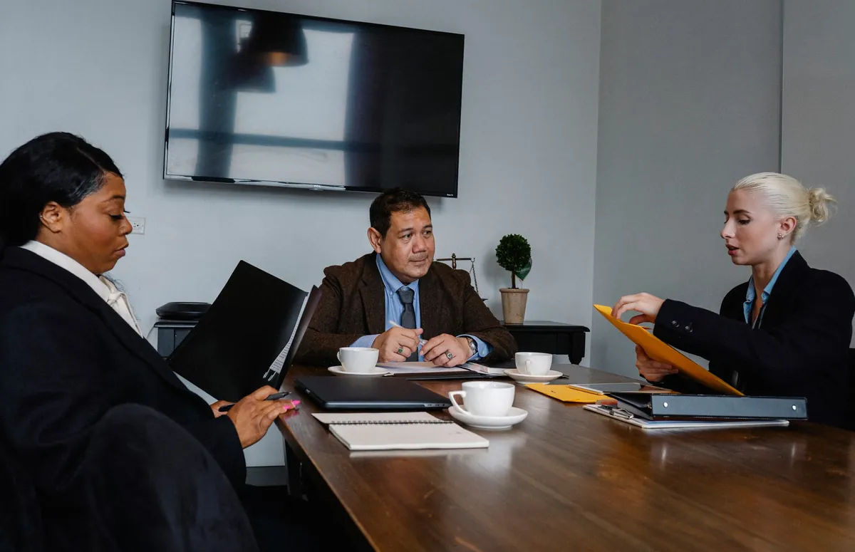 Group of multiethnic coworkers in formal wear sitting at table with documents and discussing strategy of project