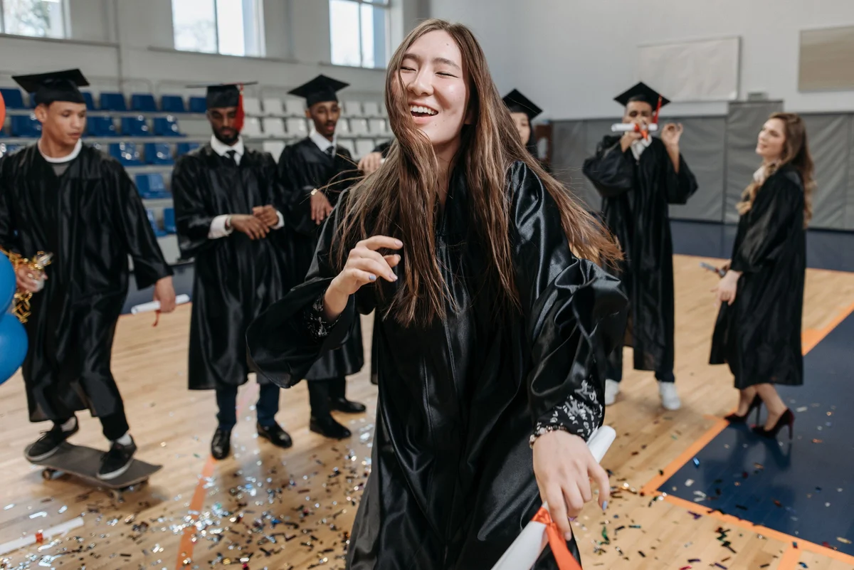 Group of diverse graduates celebrating indoors with confetti and diplomas.
